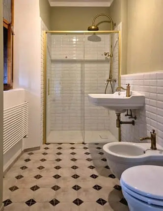 Porta doccia scorrevole profili oro installata in bagno classico con piastrelle metro bianche, lavabo colonna e rubinetteria dorata