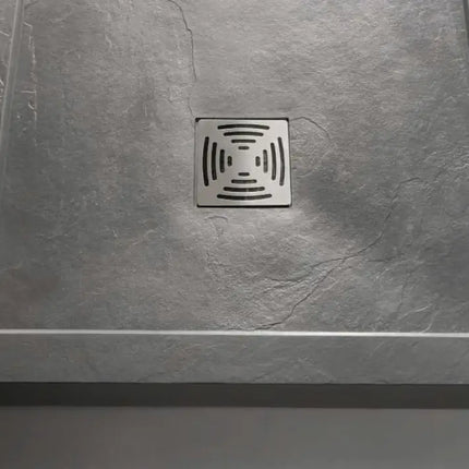 Piatto doccia grigio cemento con bordo e griglia inox quadrata installato in nicchia doccia con parete in cristallo trasparente