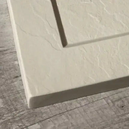 Dettaglio del bordo perimetrale rialzato del piatto doccia Flat Bordo crema, superficie effetto ardesia su pavimento in legno