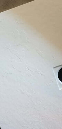Dettaglio texture superficiale effetto pietra ricomposta del piatto doccia bianco SolidStone, primo piano angolo