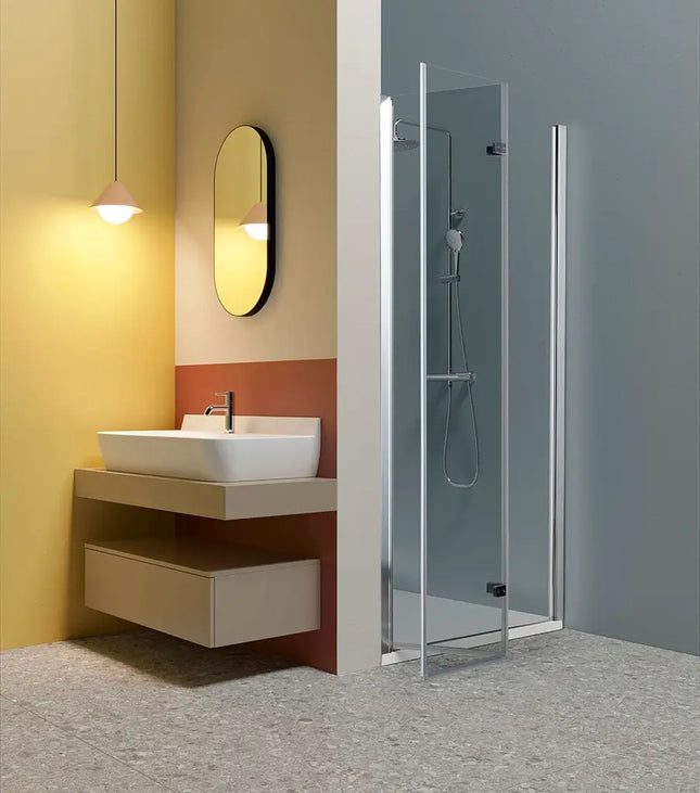 Porta doccia a libro TPS35 6mm H200cm, anta aperta verso l'esterno, in bagno luminoso con parete gialla e mobile lavabo sospeso