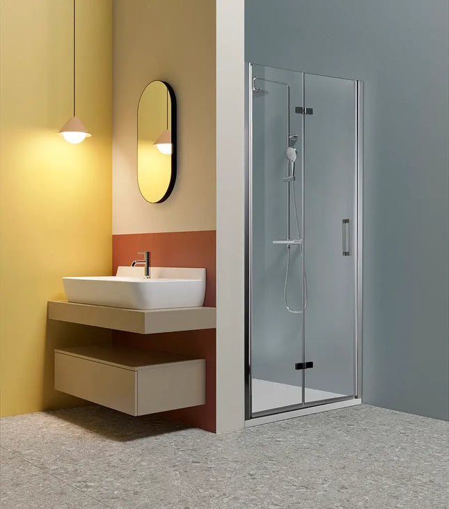 Porta doccia a libro TPS35 6mm H200cm nicchia, profili cromati, in bagno moderno con parete gialla e lavabo sospeso, anta chiusa